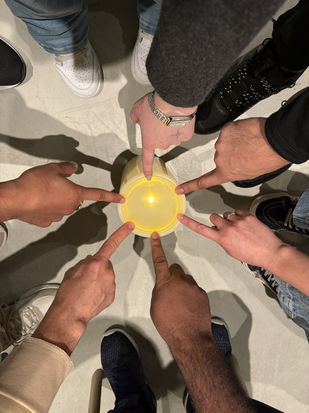Mensen in een cirkel wijzen samen naar een brandende kaars in het midden